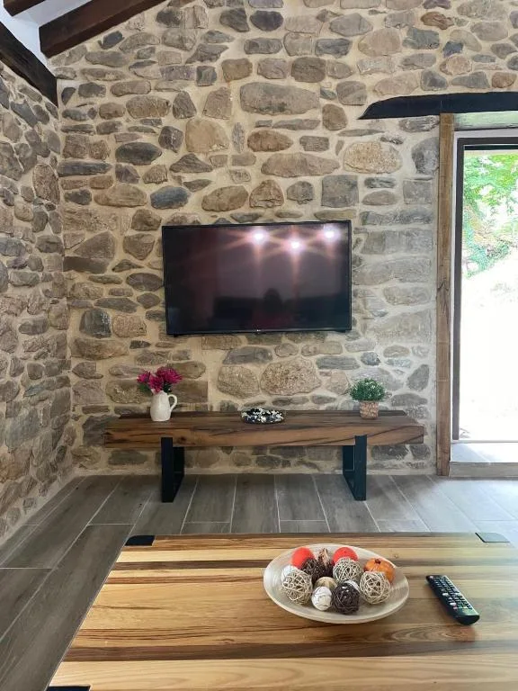 Una sala de estar con una pared de piedra con un televisor. en Cabaña Los Tejos,