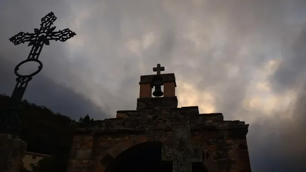 Silueta de una cruz de forja y una espadaña al atardecer